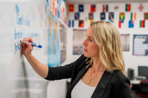 A high school teacher writing on a white board.