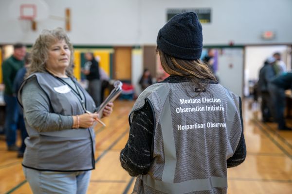 Two people wearing Montana Election Observation Initiative vests while at the polls