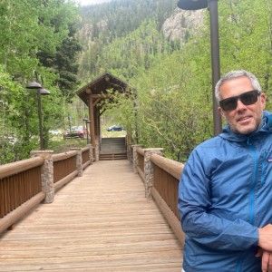 A person wearing sunglasses stands on a long wooden bridge.