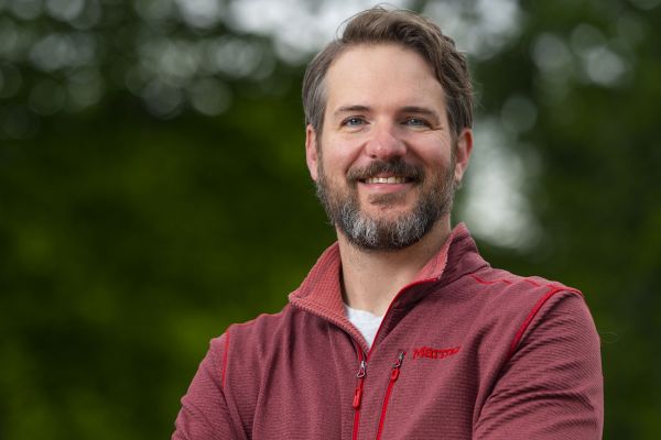 A person wearing a sweater crosses their arms and smiles widely at the camera.