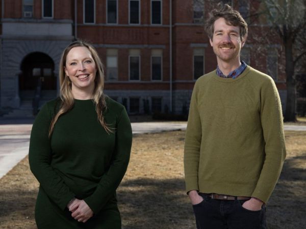 Two UM researchers stand in front of the clock tower on the oval, smiling at the camera.