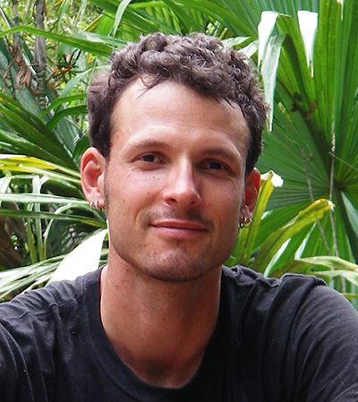 A research with piercings smiles at the camera in a jungle.