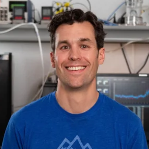 A person with curly dark hair smiles at camera.