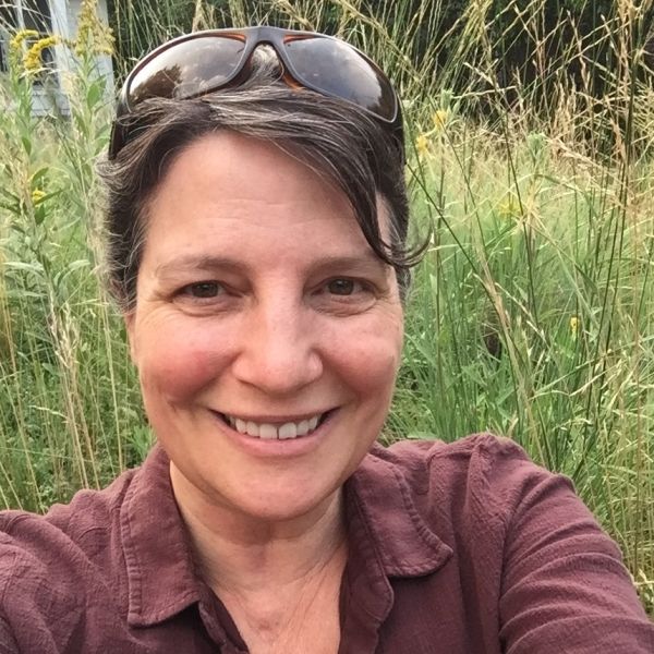 A person with pulled back grey hair smiles at the camera.