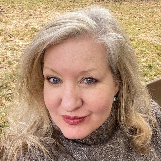 A person with light blond hair and red lipstick smiles at the camera.