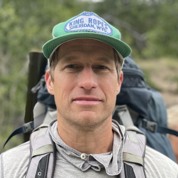 A person with a cap and backpacking gear looks at the camera.