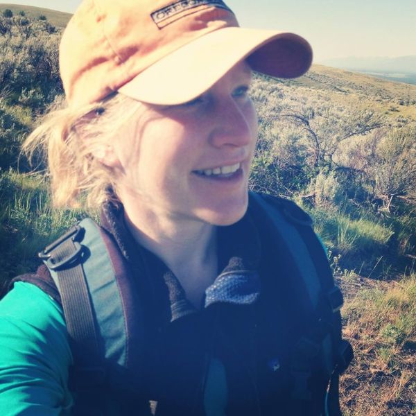A person in a cap with pulled back blond hair smiles while looking to the right.