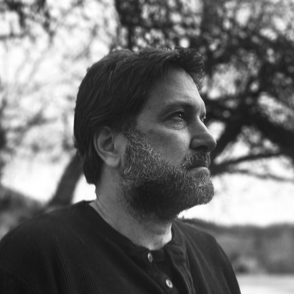 A person with a beard and medium hair stares off to the right.