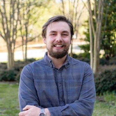 A person with a big beard crossed their arms and smiles at the camera.
