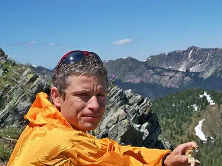 Heiko Langner in a yellow jacket looks at the camera with dramatic mountains in the background