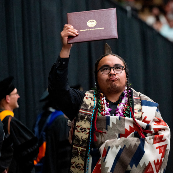 Picture of Building and Program Manger Zachariah Looking up to the crowds at graduation holding his diploma above his head