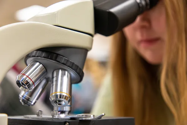 A graduate student looks into a microscope in a lab at UM
