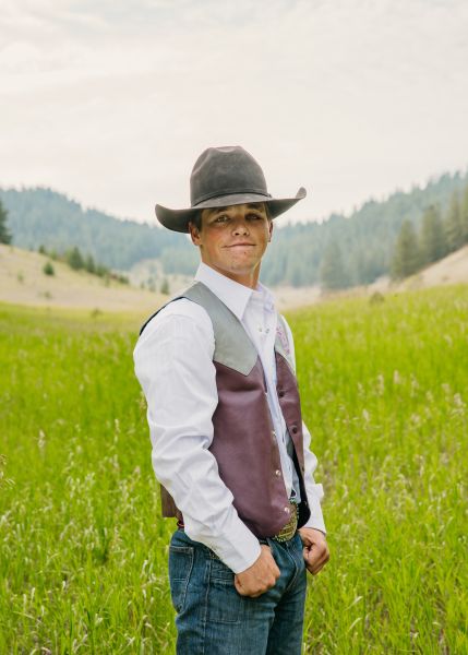 Brad McLean in Western wear stands posed with his thumbs in his pockets in a sunny field.