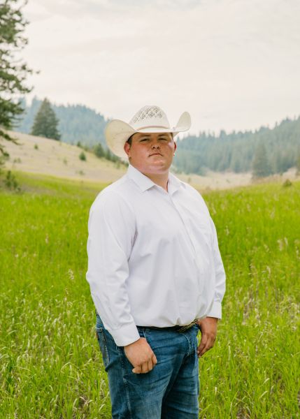 Kale Day Chief in Western wear stands posed with his thumbs in his pockets in a sunny field.