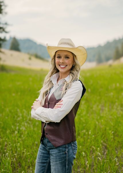 Lacey Lawrence in Western wear stands posed with her arms crossed in a sunny field.