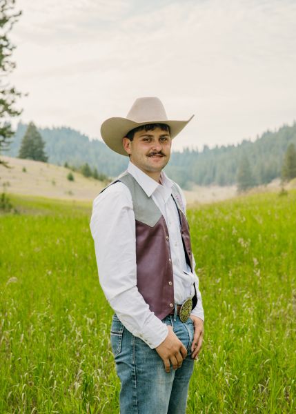 Sterling Herzog in Western wear stands posed with his thumbs in his pockets in a sunny field.