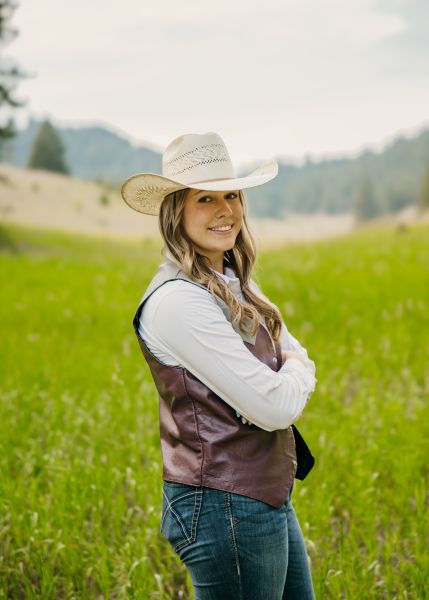 Tamara Zaugg in Western wear stands posed with her arms crossed in a sunny field.