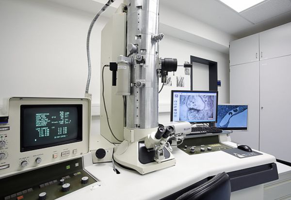 Several monitors surround a talk silver canister that resembles a microscope.