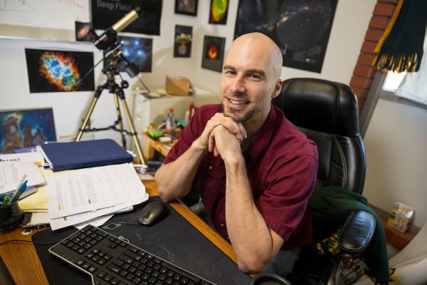 mark sits at his desk, elbows propped under his chin, solar telescope in the background
