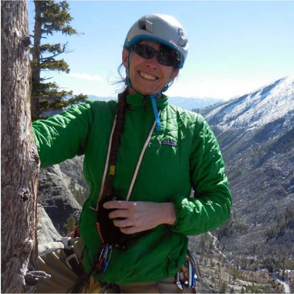 Claudine Tobalske posing by a tree with snow mountains in the background. 