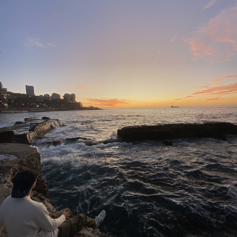 A person sitting on a rocky shoreline in Chile watching a vibrant sunset over the ocean.