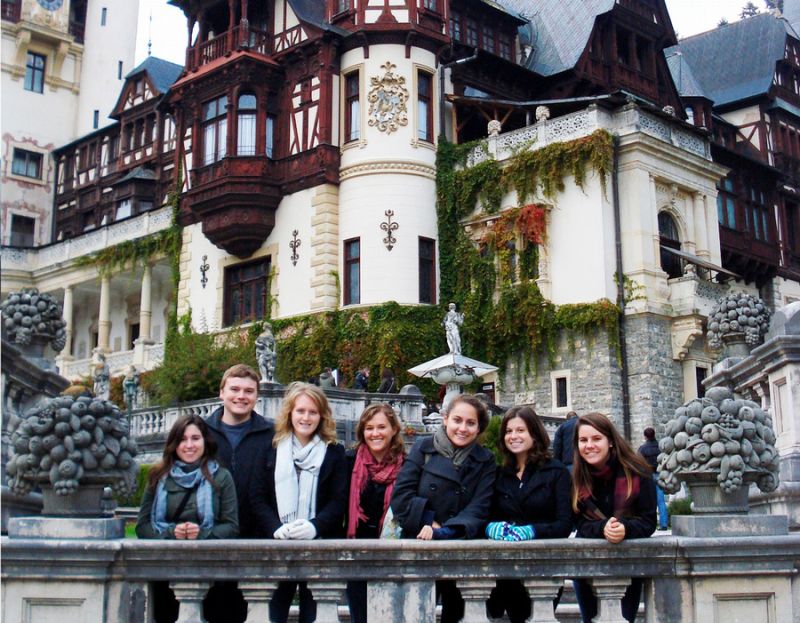 Group of seven friends posing in front of a grand, ornate building covered in greenery