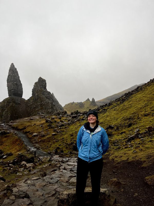 A hiker stands smiling in front of rocky spires in a misty landscape in New Zealand
