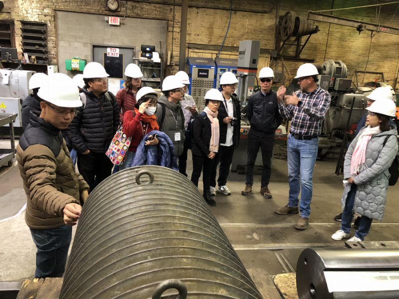 Group of individuals in hard hats engaged in a factory tour, listening to a presenter explaining machinery