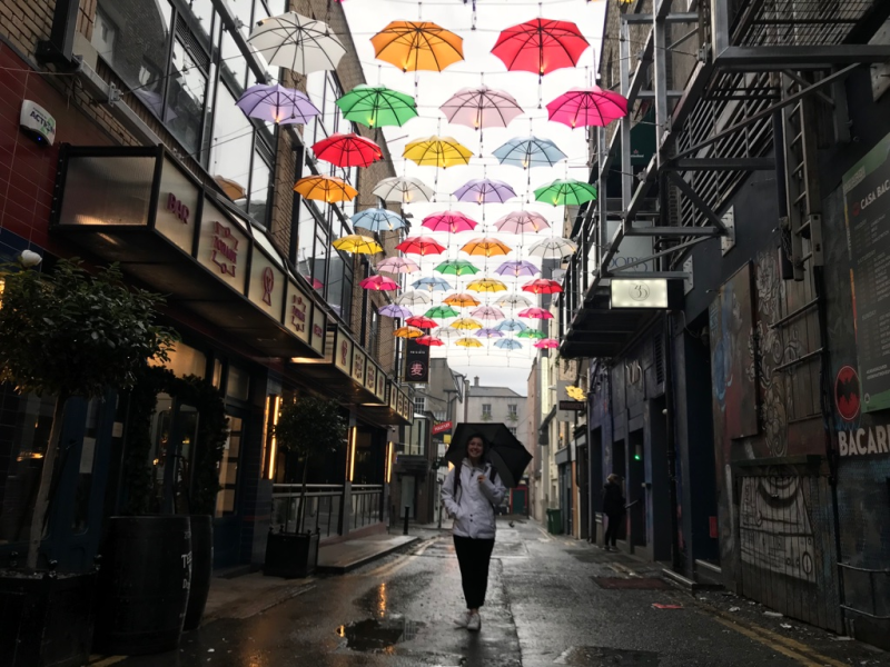 Young woman holds umbrella in an alley with fairy lights above