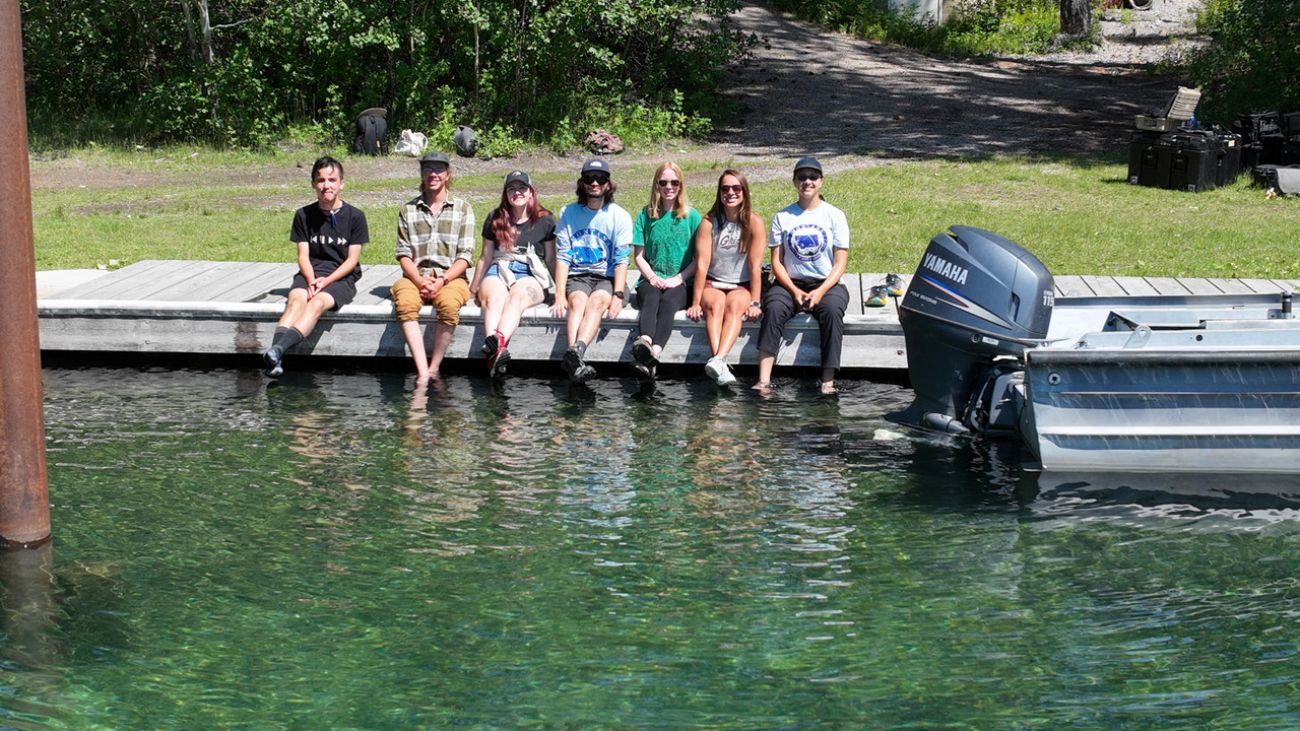 group of students sit on the dock, feet dipped in the water of Flathead Lake