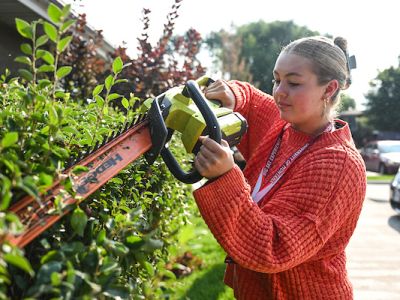A UM student helps trim shrubbery with a power tool