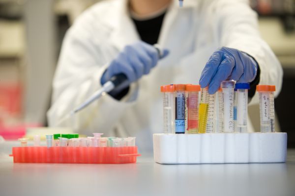 close up view of person in laboratory gear working with vials and a pipette