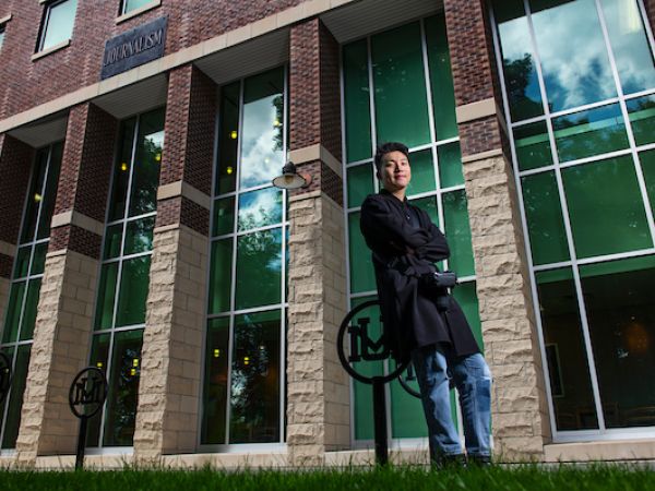 International student leans against a bike rake outside UM's journalism school