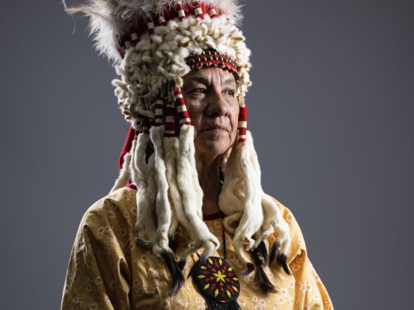 carol murray sits in front of open sky wearing an indigenous headdress