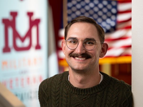 Tanner Liermann, a Marine Corps veteran, smiles for the camera. A UM banner and a US flag hang in the background