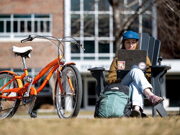 A UM student works on a laptop on the Oval. A orange bike is parked nearby