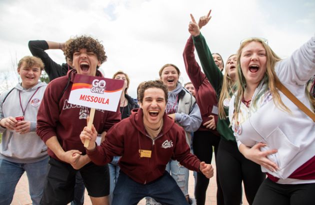 A tour guide and a group of new students enthusiastically gesture at the camera