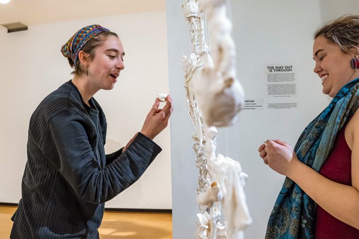 Two people admiring a curtain of small sculptures hanging from the ceiling between them