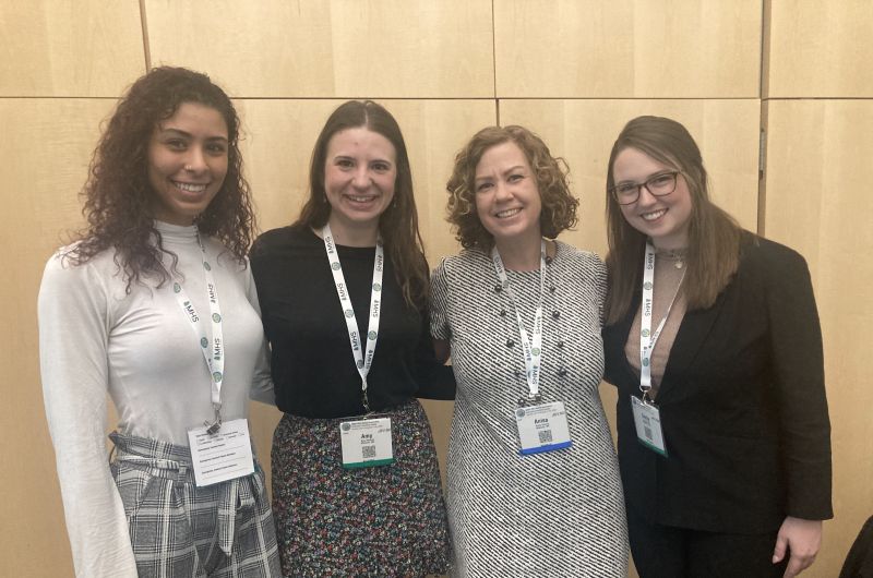 Three graduate students and Dr. Anisa Goforth standing side by side at a conference