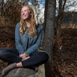 UM student Haley VonGoedert sits on a rock, looking toward her right, smiling