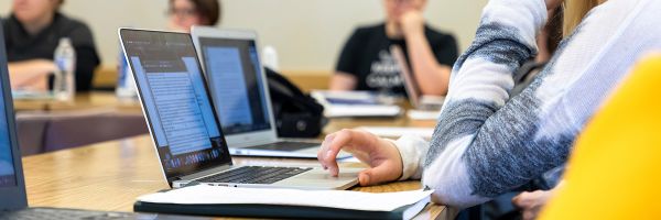 close up view of hands working on a laptop with other students in background