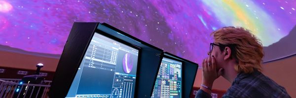 person working at the controls of a planetarium while looking up at the display