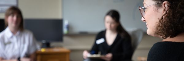 three students sitting in a circle talking, with two out of focus in the background
