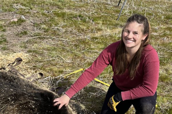Kaylie Durglo crouched down outside with one hand petting an animal