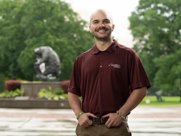 Paulo smiles for a portrait in front of the Grizzly Bear statue on the University of Montana campus.