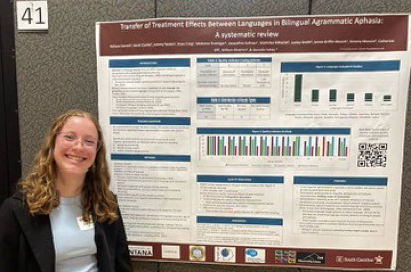 a student stands in front of her research poster