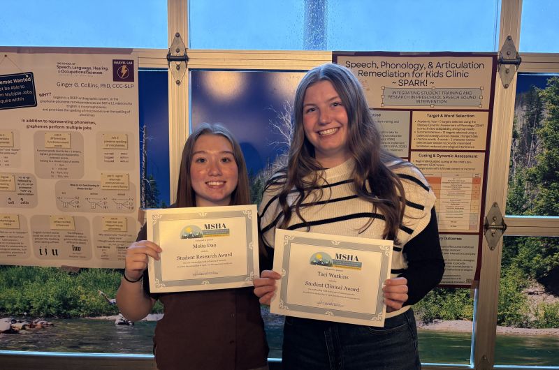 two students holding awards in front of posters. one award is for student research and the other is for student clinical.