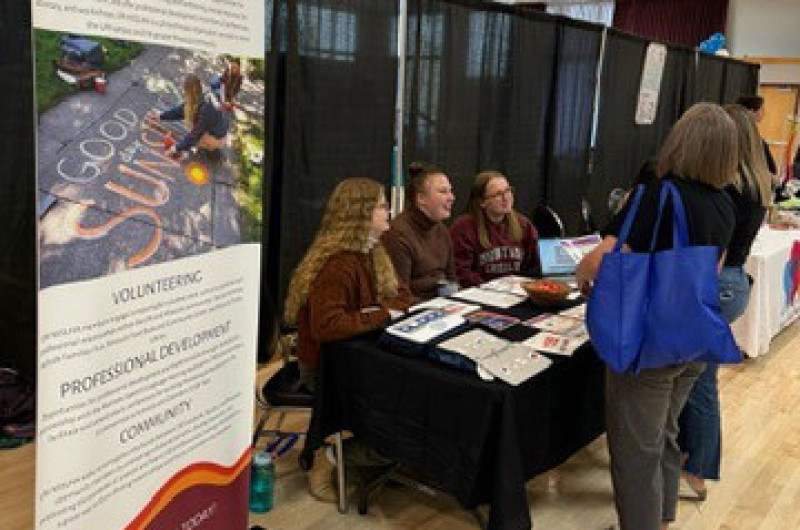 three students table at a conference. a large vertical banner on the left designates the table as NSSLHA