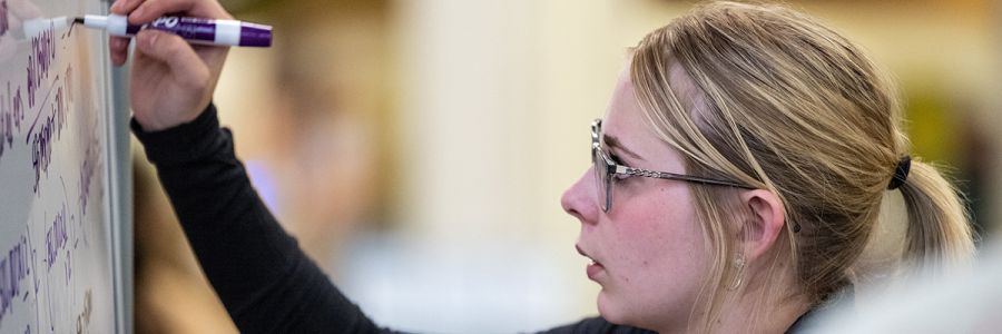student writing on a whiteboard filled with text
