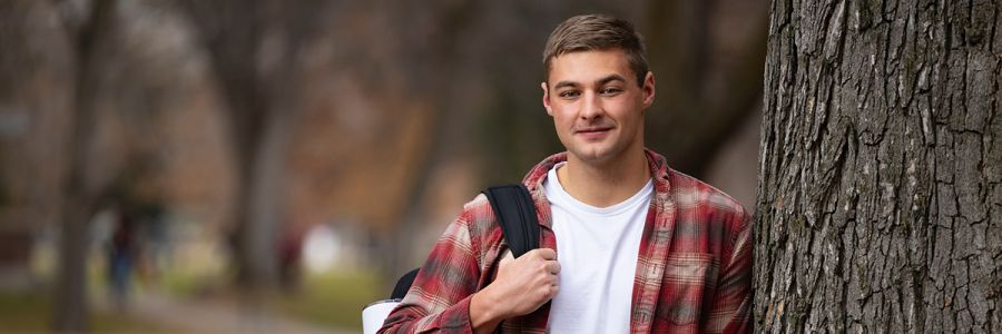 student standing outside leaning against a tree looking into the camera